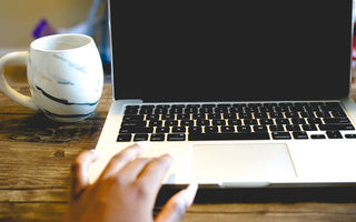 A close view of a hand on a laptop beside a marble mug on a wooden desk, ideal for remote work themes.
