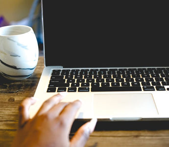 A close view of a hand on a laptop beside a marble mug on a wooden desk, ideal for remote work themes.