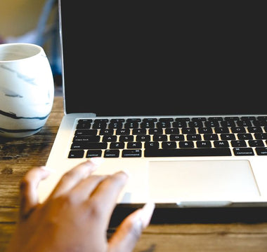 A close view of a hand on a laptop beside a marble mug on a wooden desk, ideal for remote work themes.