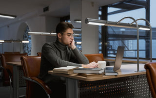 A young man deeply focused while working on a laptop in a quiet, modern library setting.