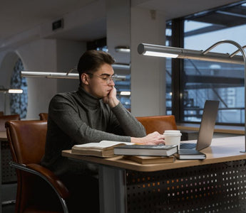 A young man deeply focused while working on a laptop in a quiet, modern library setting.
