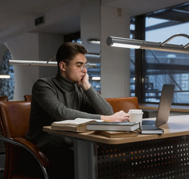 A young man deeply focused while working on a laptop in a quiet, modern library setting.