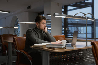 A young man deeply focused while working on a laptop in a quiet, modern library setting.