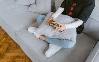 Person sitting on a couch playing video games, symbolizing leisure and entertainment.