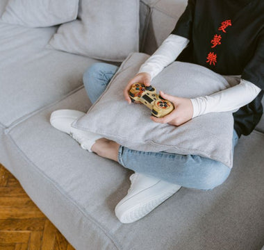 Person sitting on a couch playing video games, symbolizing leisure and entertainment.